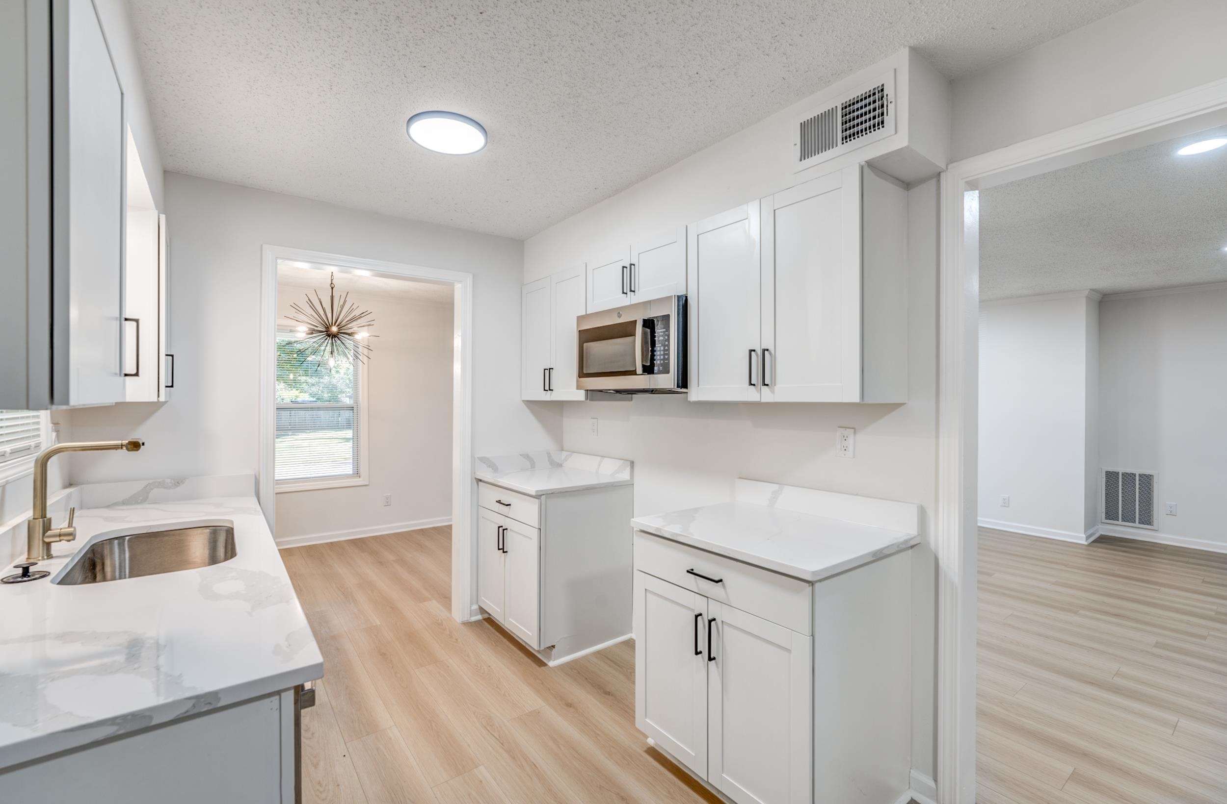 3060 Ruskin Road Bartlett, TN 38134 - Photo 11 of 30 Kitchen with a textured ceiling, light wood-type flooring, white cabinets, light stone countertops, and stainless steel microwave