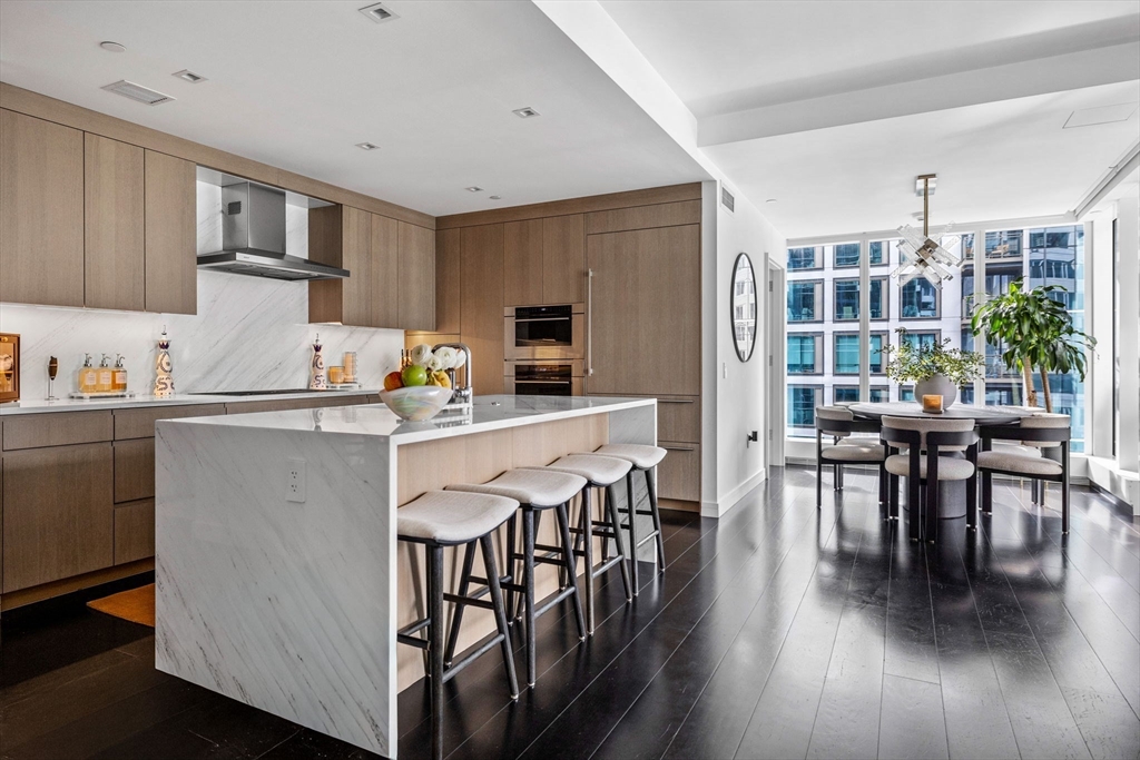 150 Seaport Boulevard, Unit 14B Boston, MA 02210 - Photo 10 of 42 a kitchen with stainless steel appliances granite countertop a stove top oven a sink a dining table and chairs with wooden floor