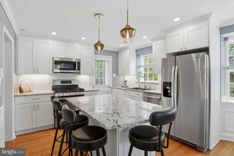 a kitchen with stainless steel appliances granite countertop a stove a refrigerator a kitchen island a dining table and chairs with wooden floor