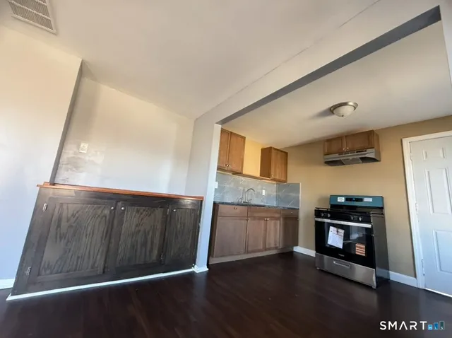 a view of a refrigerator in kitchen and an empty room with wooden floor