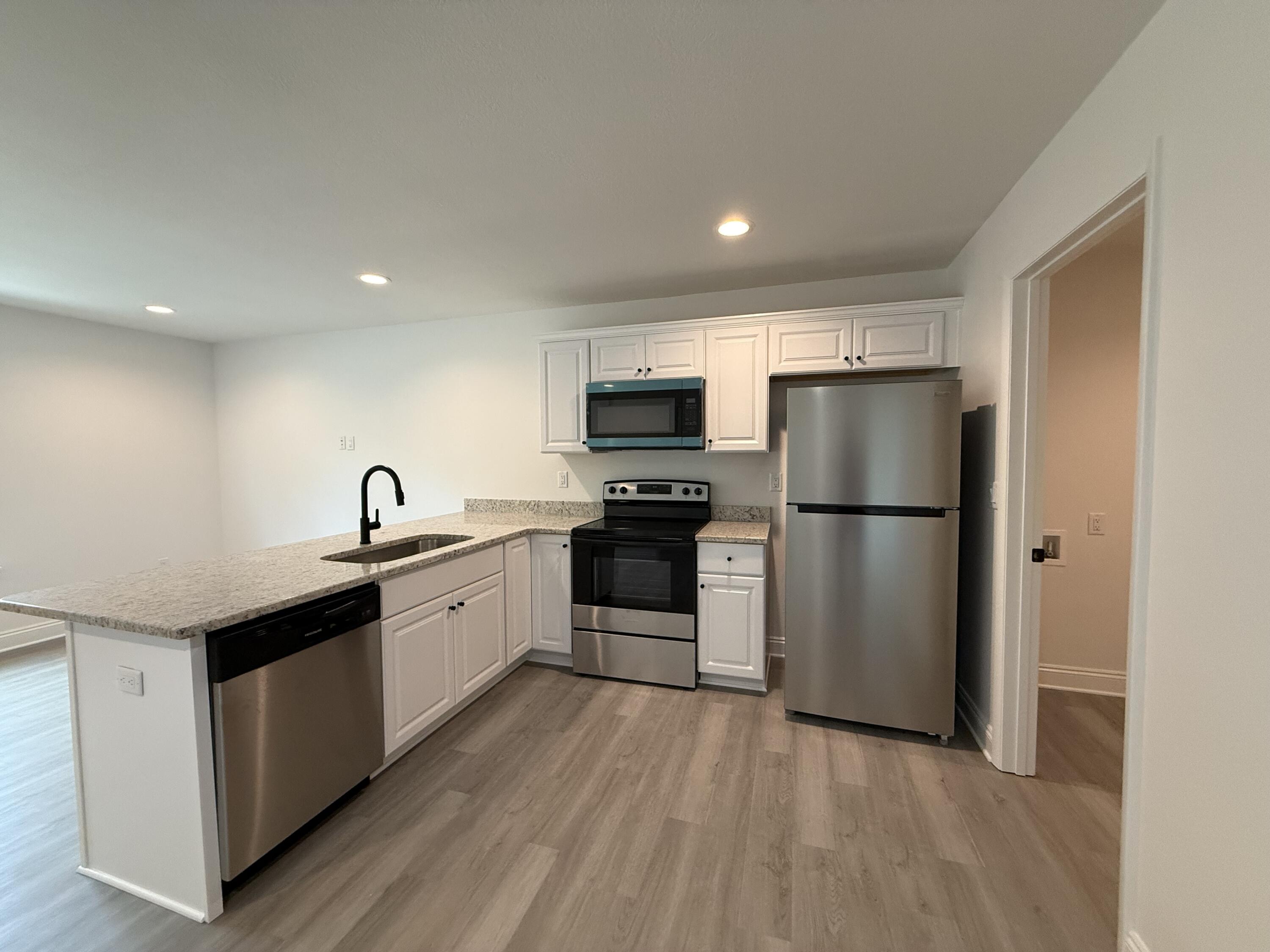 32 Constitution Avenue, Unit AB DeFuniak Springs, FL 32433 - Photo 6 of 22 a kitchen with a refrigerator a microwave oven a sink and dishwasher with wooden floor