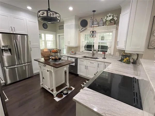 a kitchen with stainless steel appliances a stove a sink dishwasher a refrigerator white cabinets and wooden floor