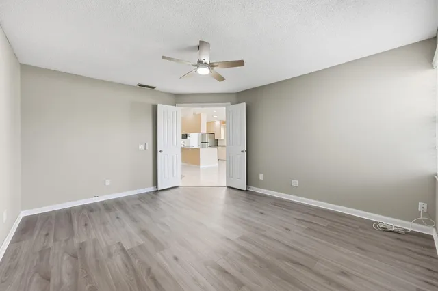 a view of an empty room with wooden floor and a ceiling fan