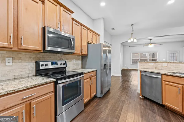 a kitchen with stainless steel appliances granite countertop a stove a sink dishwasher a refrigerator and a microwave oven with wooden floor