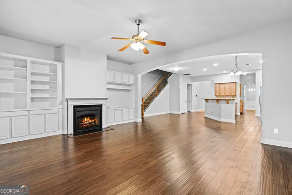 a view of an empty room with wooden floor fire place and a kitchen