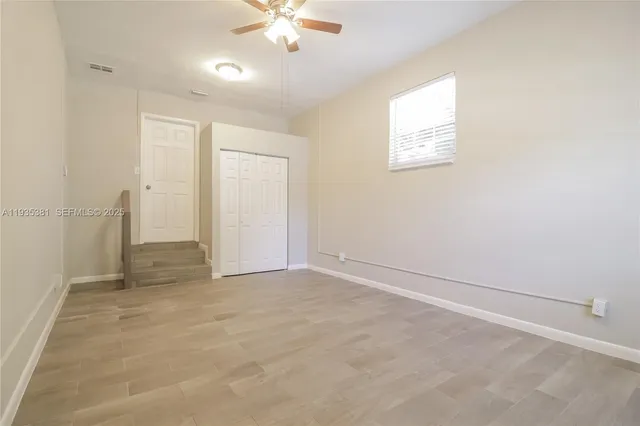 an empty room with chandelier fan and windows