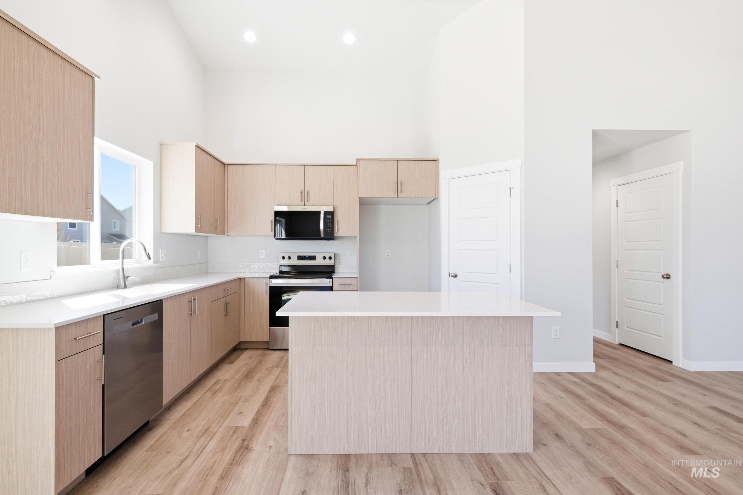 12817 Decatur Street Nampa, ID 83651 - Photo 4 of 19 Modern kitchen featuring light wood-finish cabinetry, stainless steel appliances, a white tile backsplash, and a central island with a white countertop