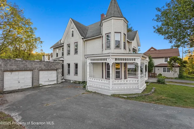 a view of a white house with a large window and a yard with plants and large trees