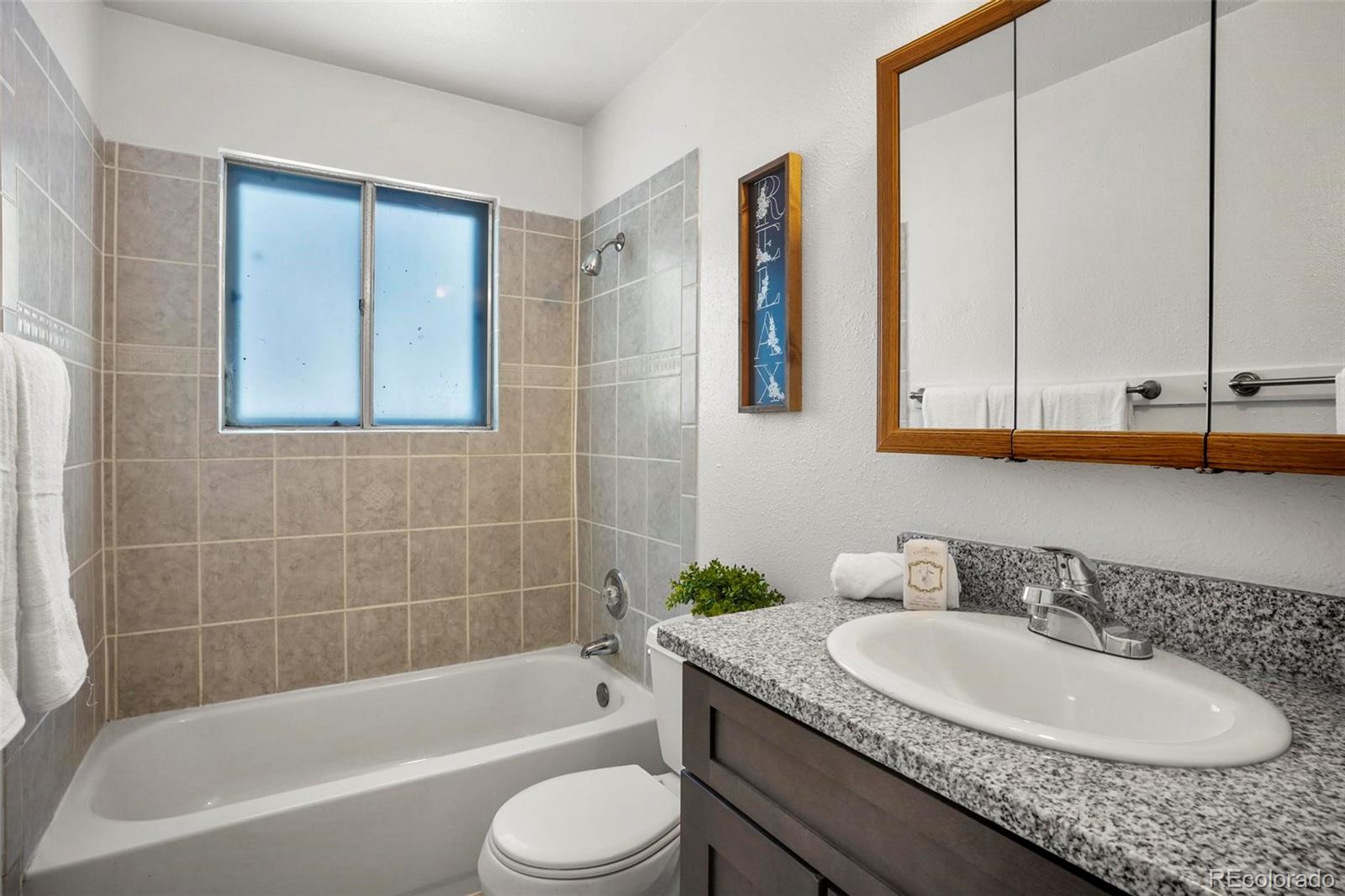 5522 Carson Street Denver, CO 80239 - Photo 22 of 40 a bathroom with a granite countertop sink a toilet and bathtub