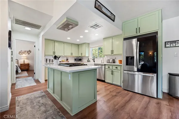 a kitchen with stainless steel appliances granite countertop a refrigerator a sink dishwasher a stove and white cabinets with wooden floor