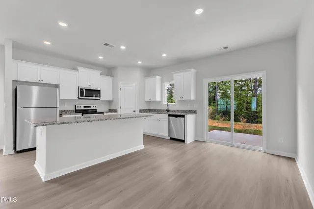 a kitchen with stainless steel appliances granite countertop a refrigerator a sink dishwasher a stove and white cabinets with wooden floor