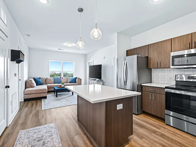 a kitchen with stainless steel appliances granite countertop a refrigerator a stove a sink dishwasher and a dining table with wooden floor