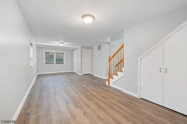 a view of an empty room with wooden floor and stairs