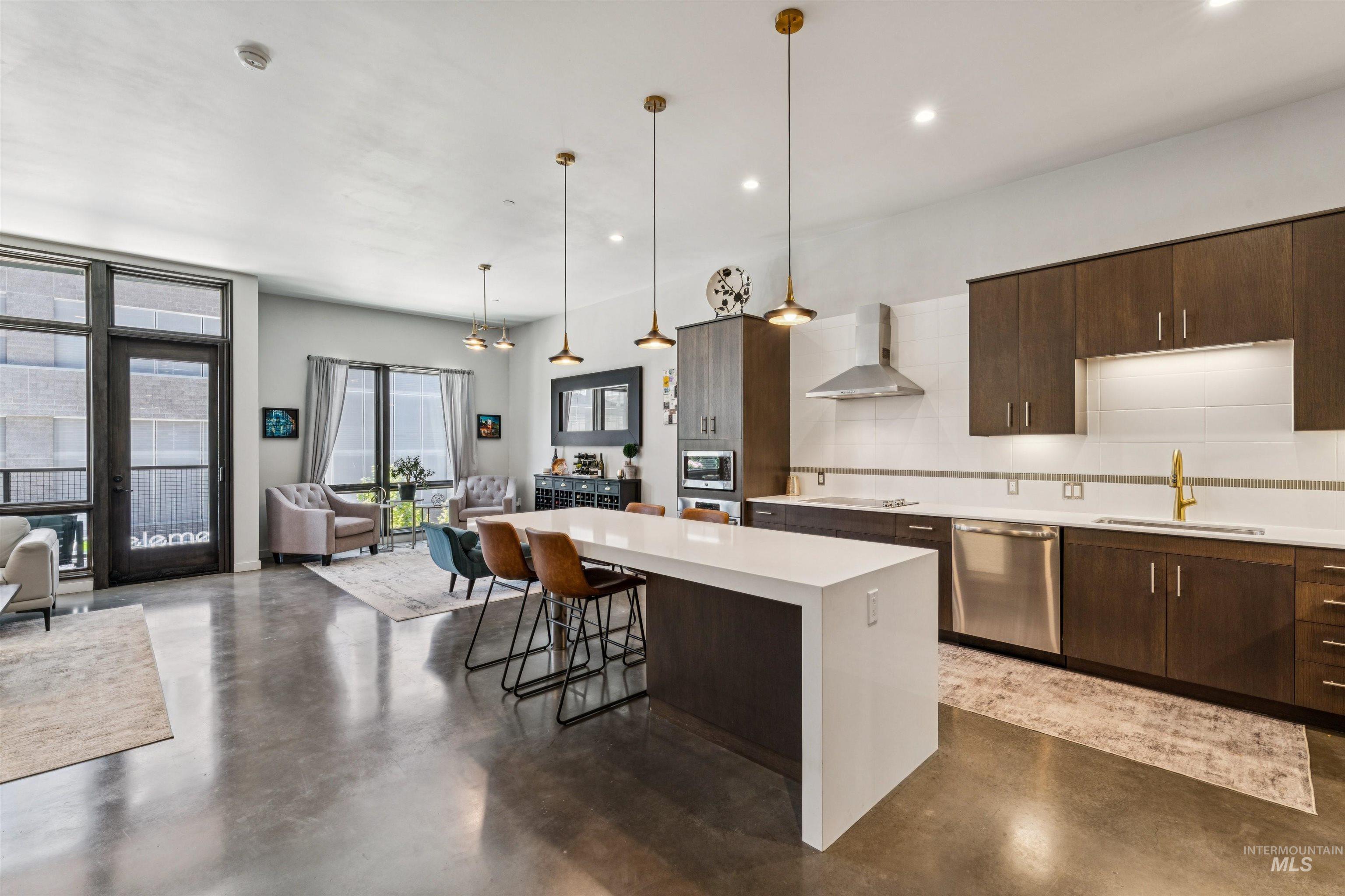 119 South 10th Street, Unit 307 Boise, ID 83702 - Photo 8 of 47 Open-concept living space featuring polished concrete flooring, a large kitchen island with a white countertop, dark wood-finish cabinetry, stainless steel appliances, and a glass-paneled door to an outdoor area