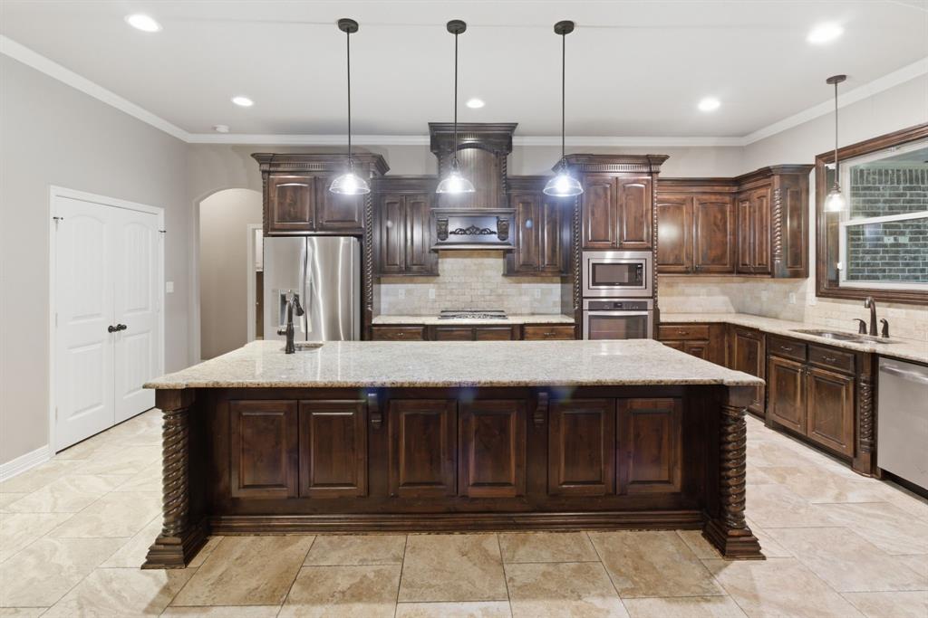 7765 Hickory Spring Lane Tyler, TX 75703 - Photo 17 of 38 Kitchen featuring a large central island with pendant lighting, rich wood cabinetry, stainless steel appliances, light-colored countertops, and a complementary tile backsplash
