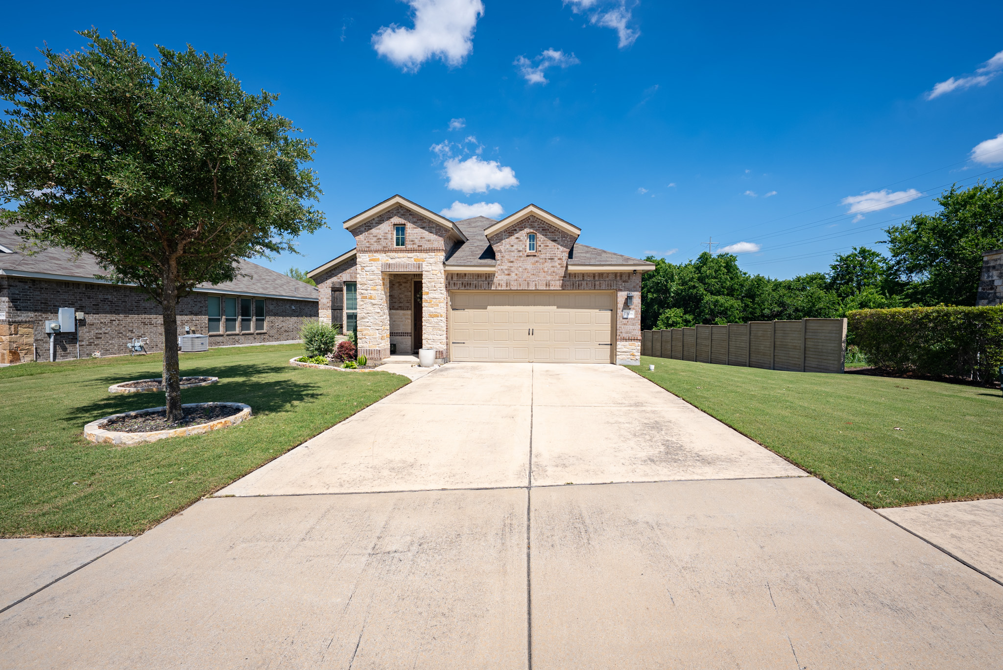 2508 Hat Bender Loop Round Rock, TX 78664 - Photo 1 of 22 Brick and stone exterior featuring a two-car garage, concrete driveway, manicured lawn, and mature landscaping