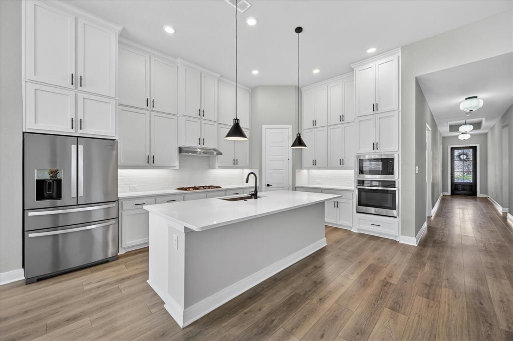 2237 Pika Road Northlake, TX 76247 - Photo 10 of 37 Kitchen featuring white shaker-style cabinetry, stainless steel appliances, a center island with a sink, and wood-finish flooring