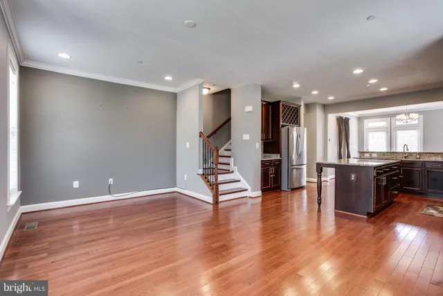a view of an empty room with wooden floor and a kitchen