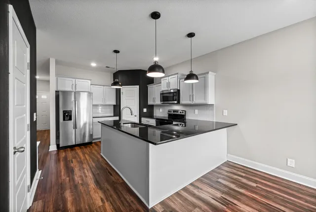 a kitchen with stainless steel appliances granite countertop a sink a stove a refrigerator and island with wooden floor