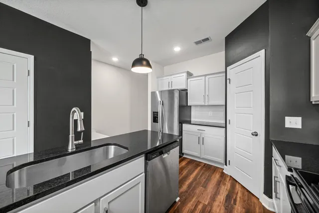 a kitchen with stainless steel appliances granite countertop a refrigerator a sink and white cabinets