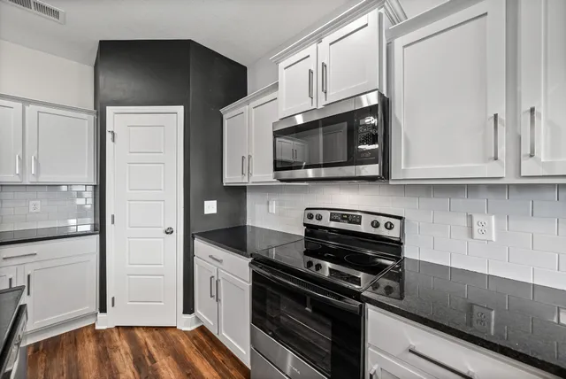 a kitchen with stainless steel appliances granite countertop white cabinets and black stove top oven with granite countertops