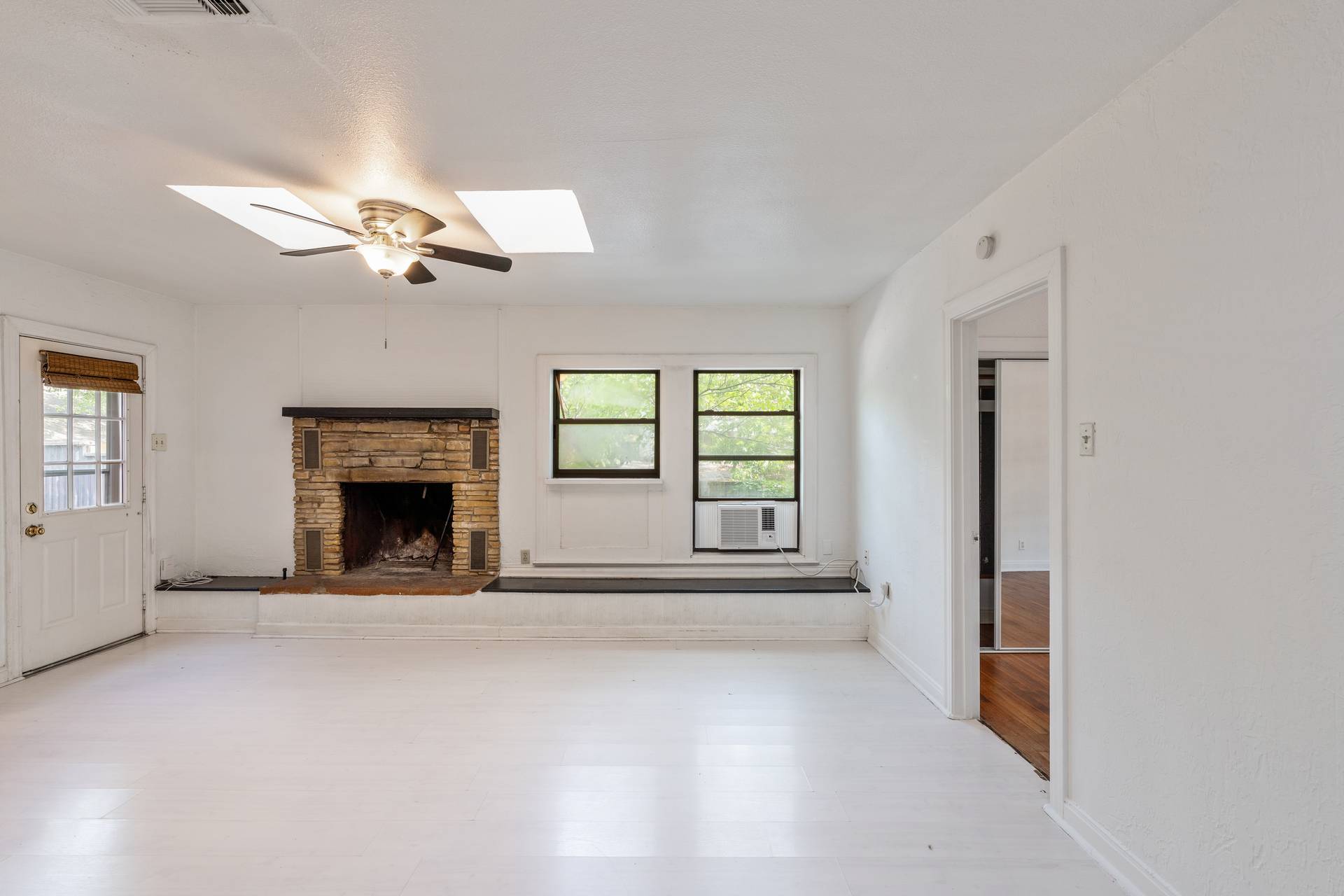 406 East Monroe Street, Unit B Austin, TX 78704 - Photo 18 of 35 Unfurnished living room with wood finished floors, a stone fireplace, a skylight, ceiling fan, and cooling unit