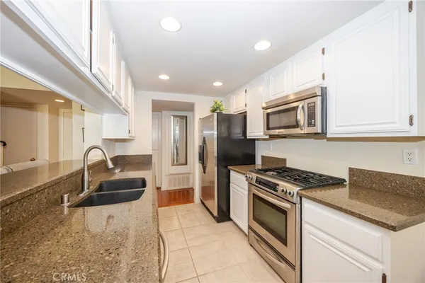 a kitchen with granite countertop stainless steel appliances a stove a sink a microwave a refrigerator and cabinets