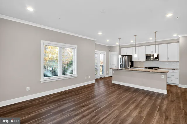 a large kitchen with stainless steel appliances granite countertop a large window a oven and white cabinets with wooden floor