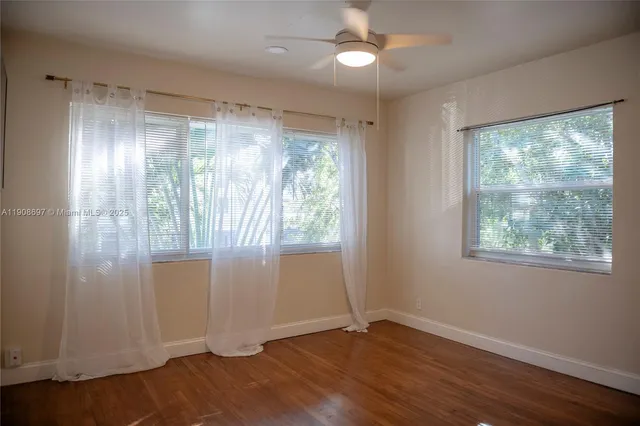 an empty room with wooden floor fan and windows