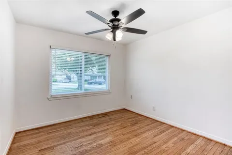 an empty room with wooden floor chandelier fan and windows