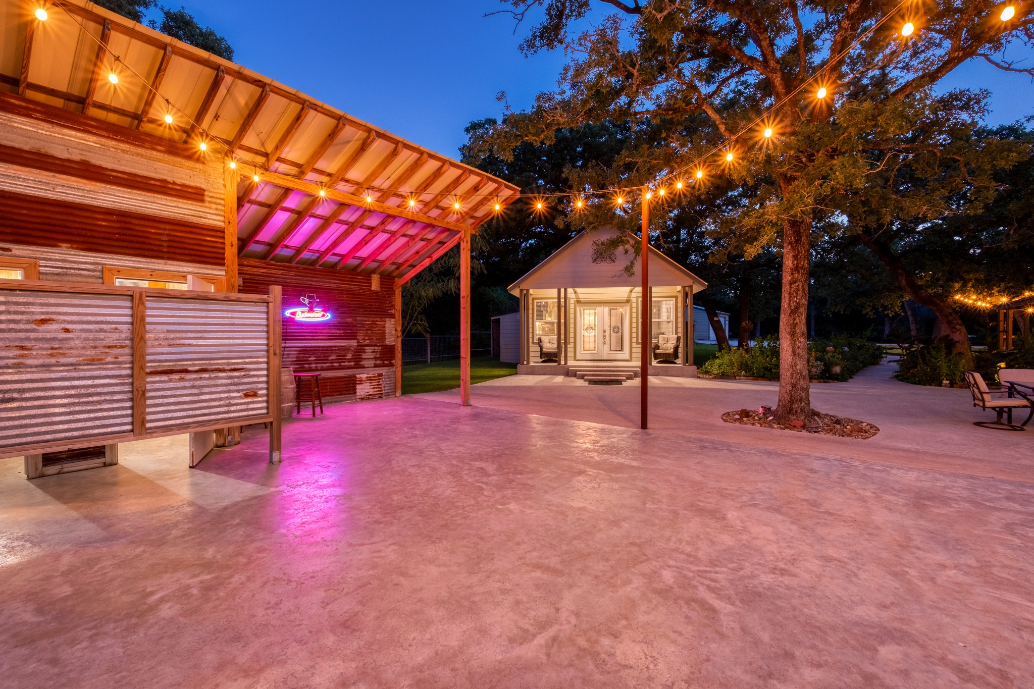 1474 County Rd B Lexington, TX 78947 - Photo 20 of 34 Illuminated strings of lights create a festive atmosphere across the paved outdoor area and between the two charming structures.
