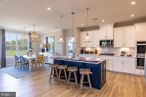 a kitchen with stainless steel appliances granite countertop a stove a refrigerator a kitchen island a dining table and chairs with wooden floor