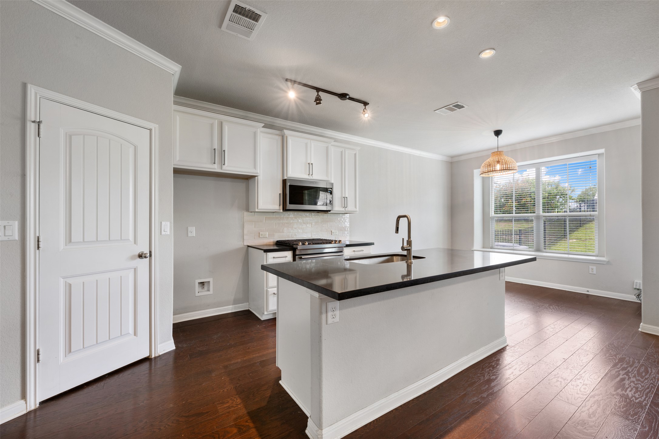 211 Parable Cove Pflugerville, TX 78660 - Photo 9 of 40 Open-concept kitchen featuring an island with a built-in sink, white cabinetry, integrated microwave, and dark wood-finish flooring