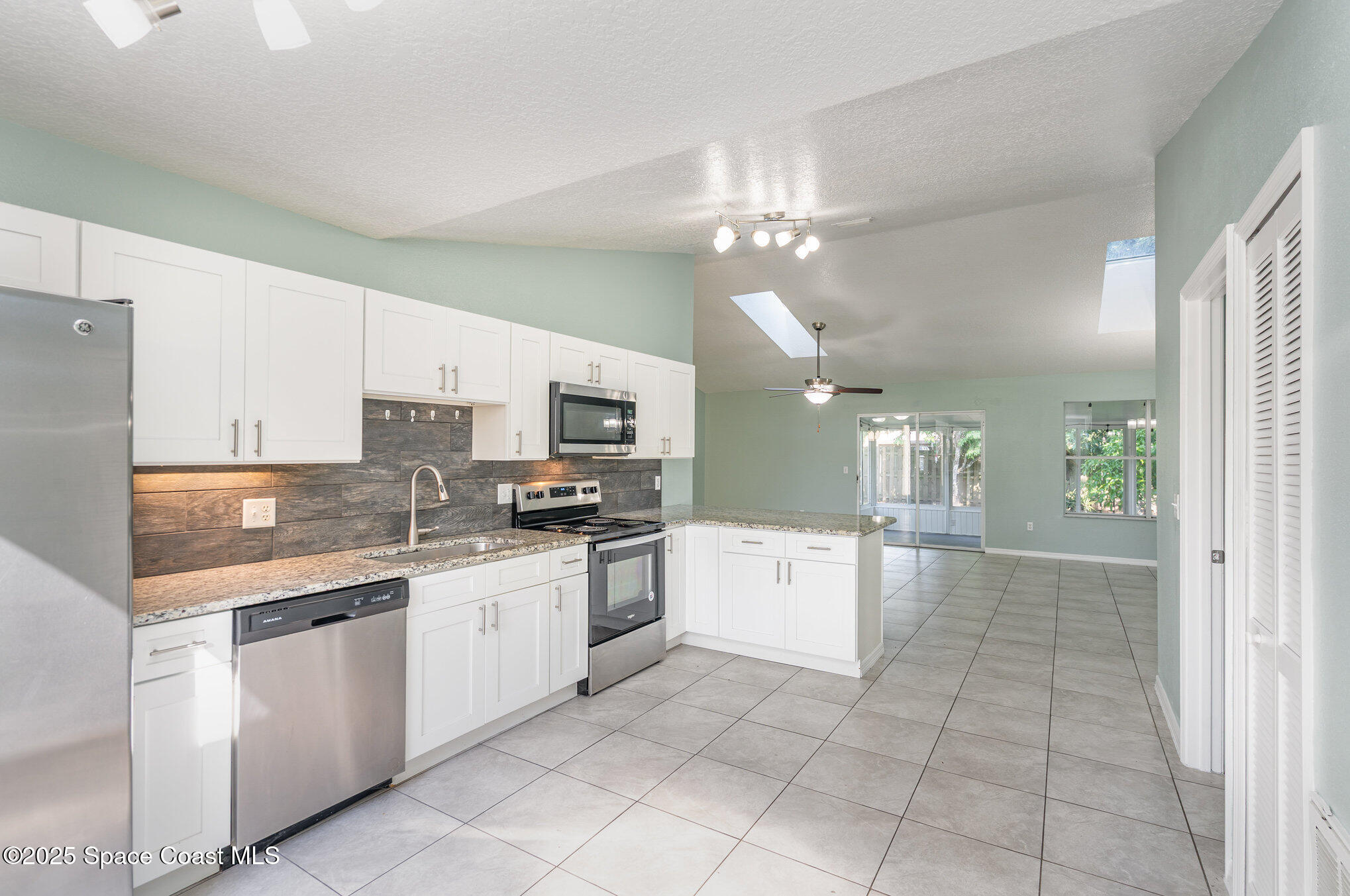 636 Fishtail Palm Boulevard Melbourne, FL 32901 - Photo 11 of 25 a large white kitchen with stainless steel appliances granite countertop a stove top oven a sink dishwasher and white cabinets next to a window