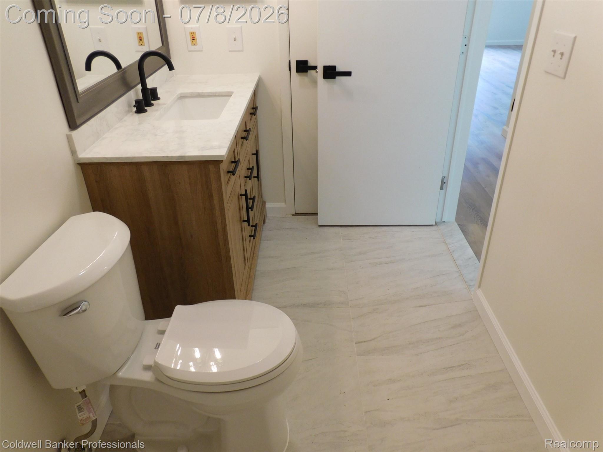 284 East 13 Mile Road Madison Heights, MI 48071 - Photo 15 of 21 Bathroom featuring a wood-finish vanity with a white countertop and integrated sink, matte black faucet, and a wall-mounted mirror