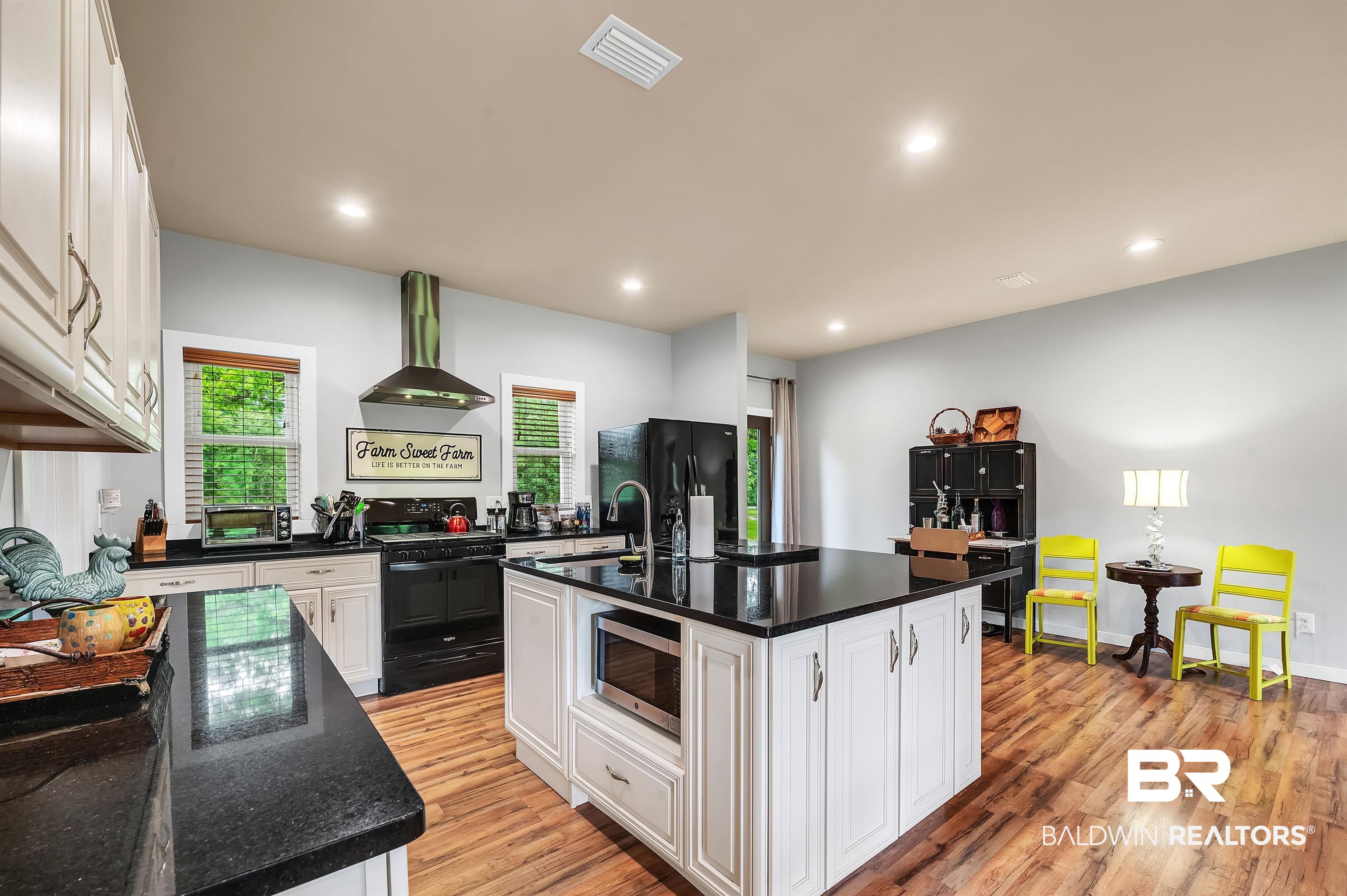 13827 County Road 83 Elberta, AL 36530 - Photo 20 of 38 Kitchen with black appliances, wall chimney range hood, a center island with sink, white cabinetry, and light wood-style floors