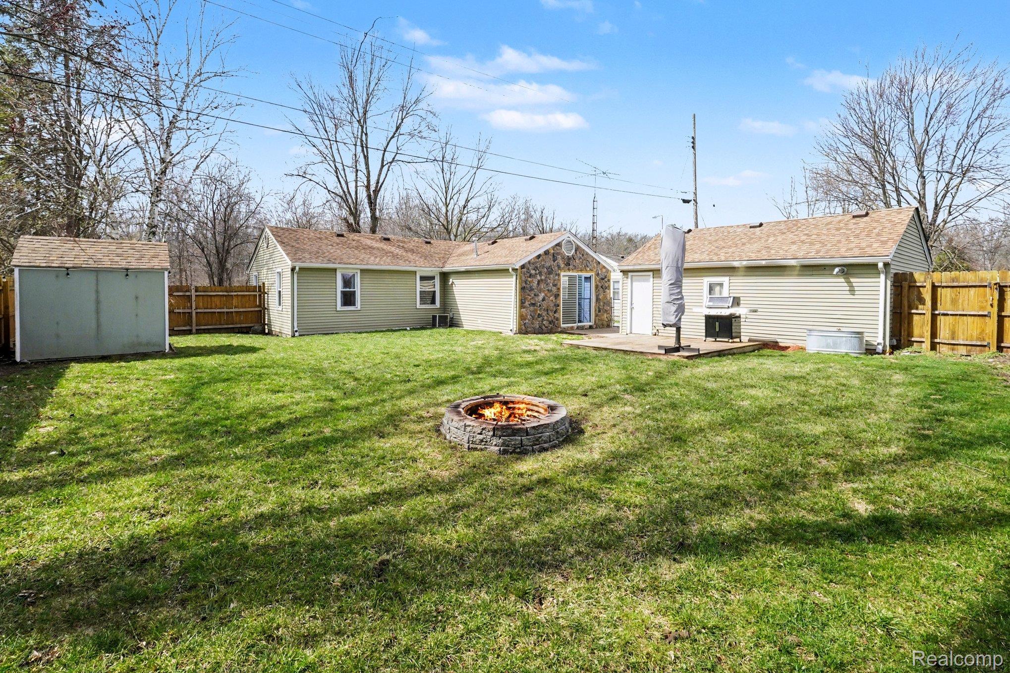 16485 Jennings Road Fenton, MI 48430 - Photo 6 of 27 Rear view of property with a fenced backyard, an outdoor fire pit, a storage unit, and a patio
