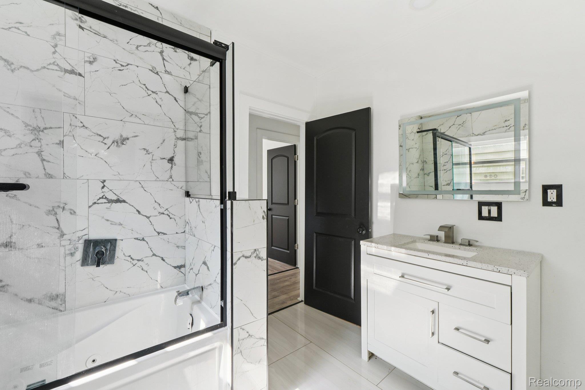 16210 Inverness Street Detroit, MI 48221 - Photo 16 of 29 Bathtub with clear glass enclosure, marble-style tiled walls, and a wall-mounted shower fixture