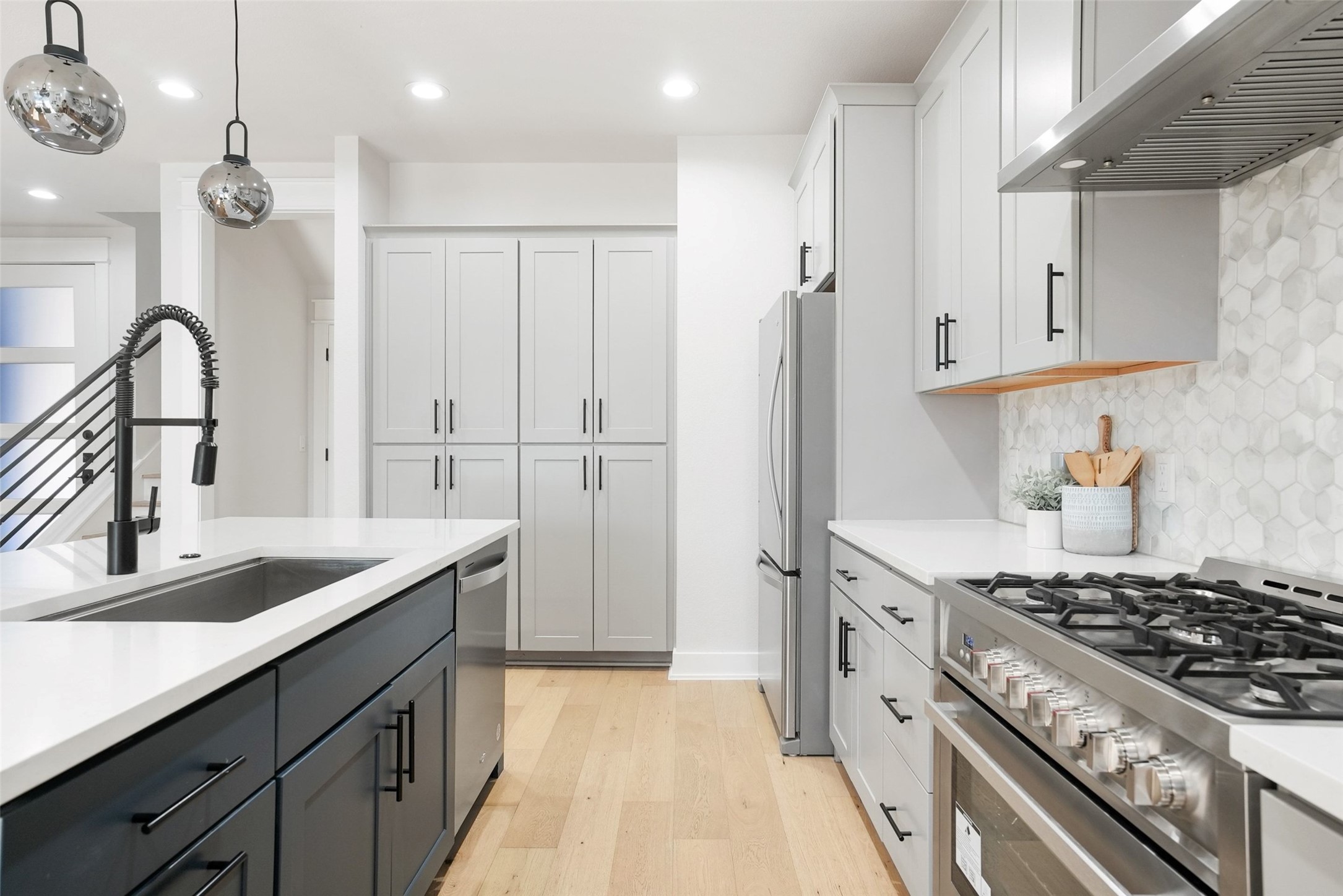 5109 Stone Gate Drive, Unit 2 Austin, TX 78721 - Photo 6 of 36 Modern kitchen featuring a stainless steel range with hood, hexagon tile backsplash, light wood-finish flooring, white countertops, and a kitchen island with an undermount sink and black faucet