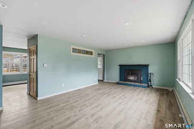 an empty room with wooden floor fire place and windows