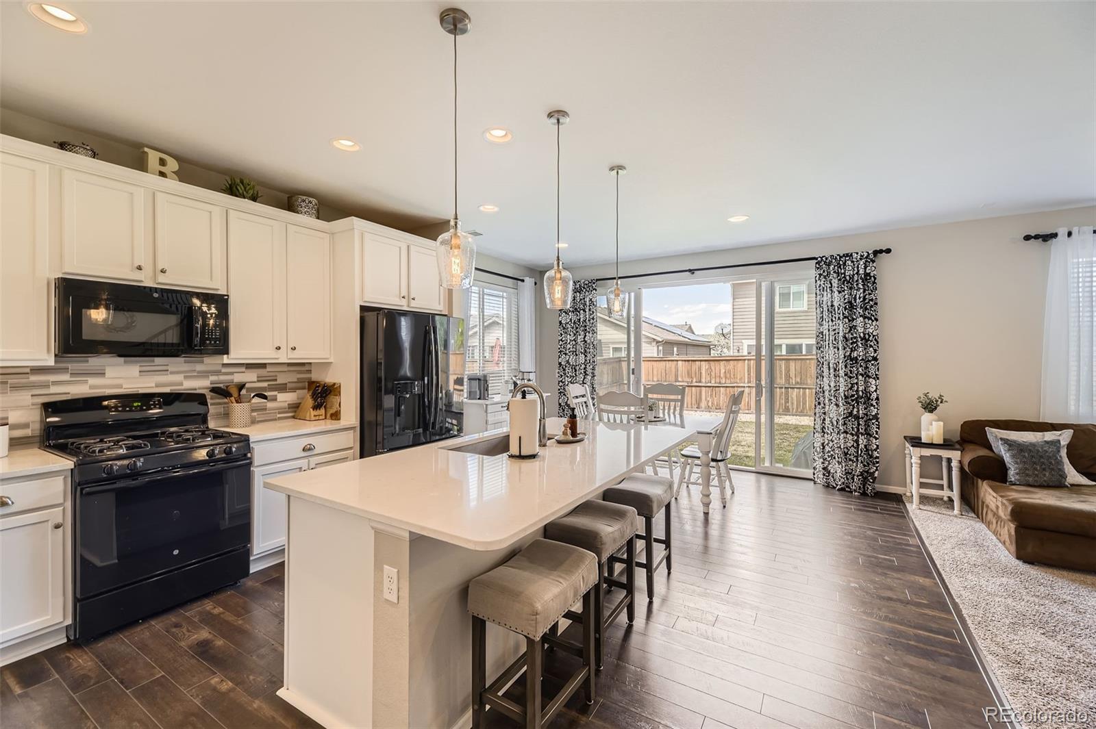 25621 East Cedar Place Aurora, CO 80018 - Photo 4 of 30 a kitchen with stainless steel appliances a stove a refrigerator a kitchen island a stove and a dining table with wooden floor