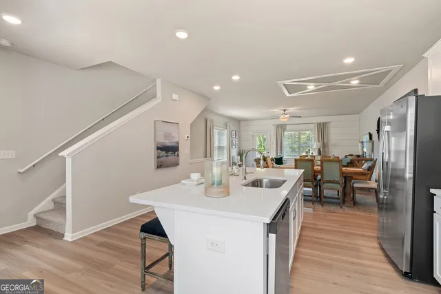 a kitchen with stainless steel appliances kitchen island granite countertop a refrigerator a sink a stove and a dining table with wooden floor