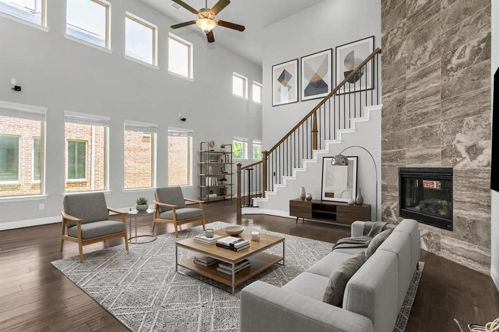 6333 Hall Road Frisco, TX 75034 - Photo 11 of 38 Two-story living area featuring a stone-clad fireplace, dark wood-finish flooring, a contemporary staircase with iron balusters, a ceiling fan, and multiple windows