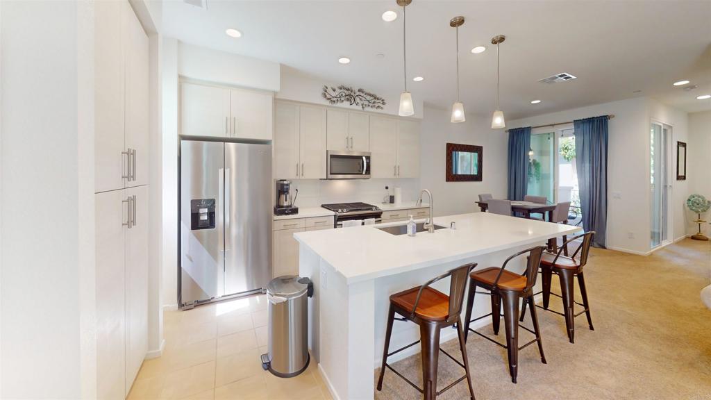 1150 Via Lucero Oceanside, CA 92056 - Photo 2 of 11 a kitchen with stainless steel appliances kitchen island granite countertop a dining table chairs refrigerator and microwave