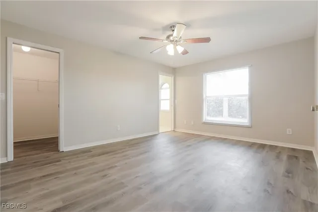an empty room with wooden floor chandelier fan and windows