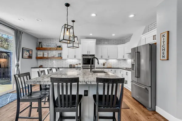 a kitchen with stainless steel appliances granite countertop a dining table chairs and white cabinets