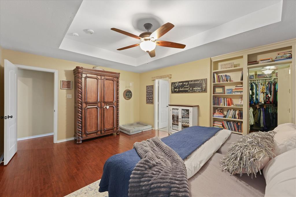 112 Springfield Lane Red Oak, TX 75165 - Photo 16 of 40 Spacious primary bedroom featuring wood-finish flooring, a tray ceiling with a ceiling fan, a built-in bookshelf, and a hidden walk-in closet with interior lighting