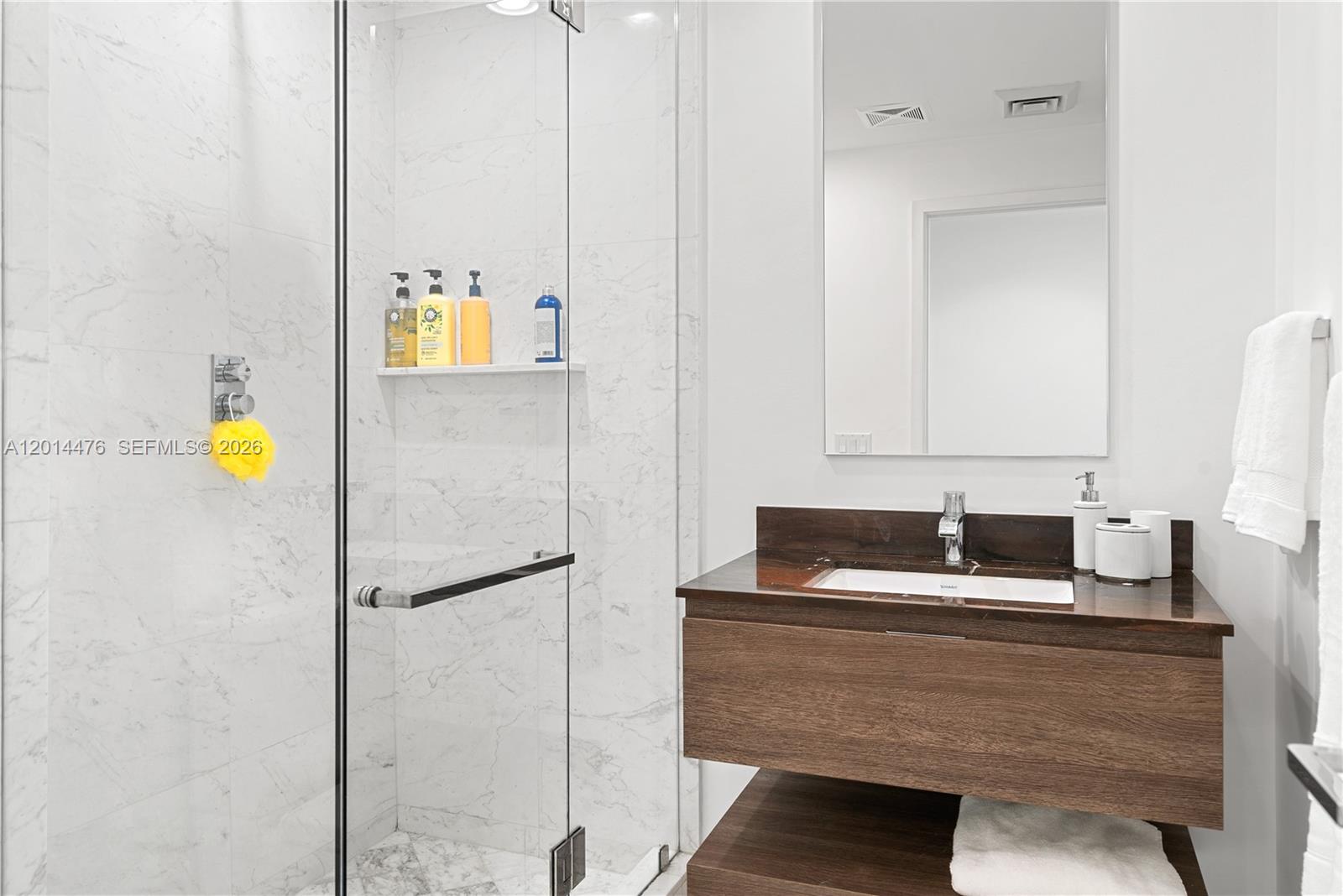 360 Ocean Drive, Unit 1106S Key Biscayne, FL 33149 - Photo 20 of 67 Guest Bathroom – The guest bathroom offers a glass-enclosed shower with marble-look tile, a floating wood vanity, and a dark stone countertop. Bright lighting and minimalist details create a fresh, contemporary design.