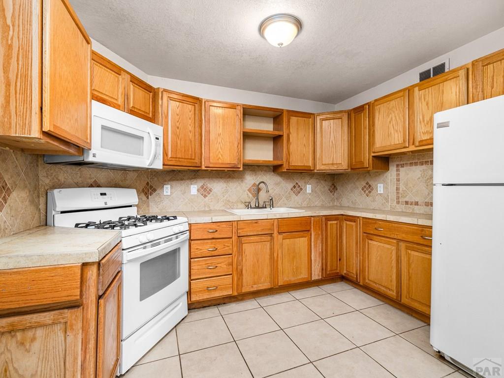 2610 Azalea Street Pueblo, CO 81005 - Photo 7 of 19 a kitchen with stainless steel appliances granite countertop a stove a sink and white cabinets