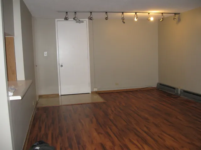 an empty room with chandelier fan and kitchen view